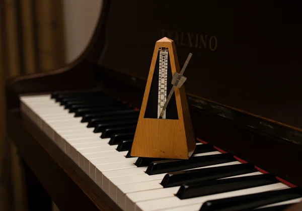 Ein klassisches Metronom mit einem Klavier im Hintergrund.
